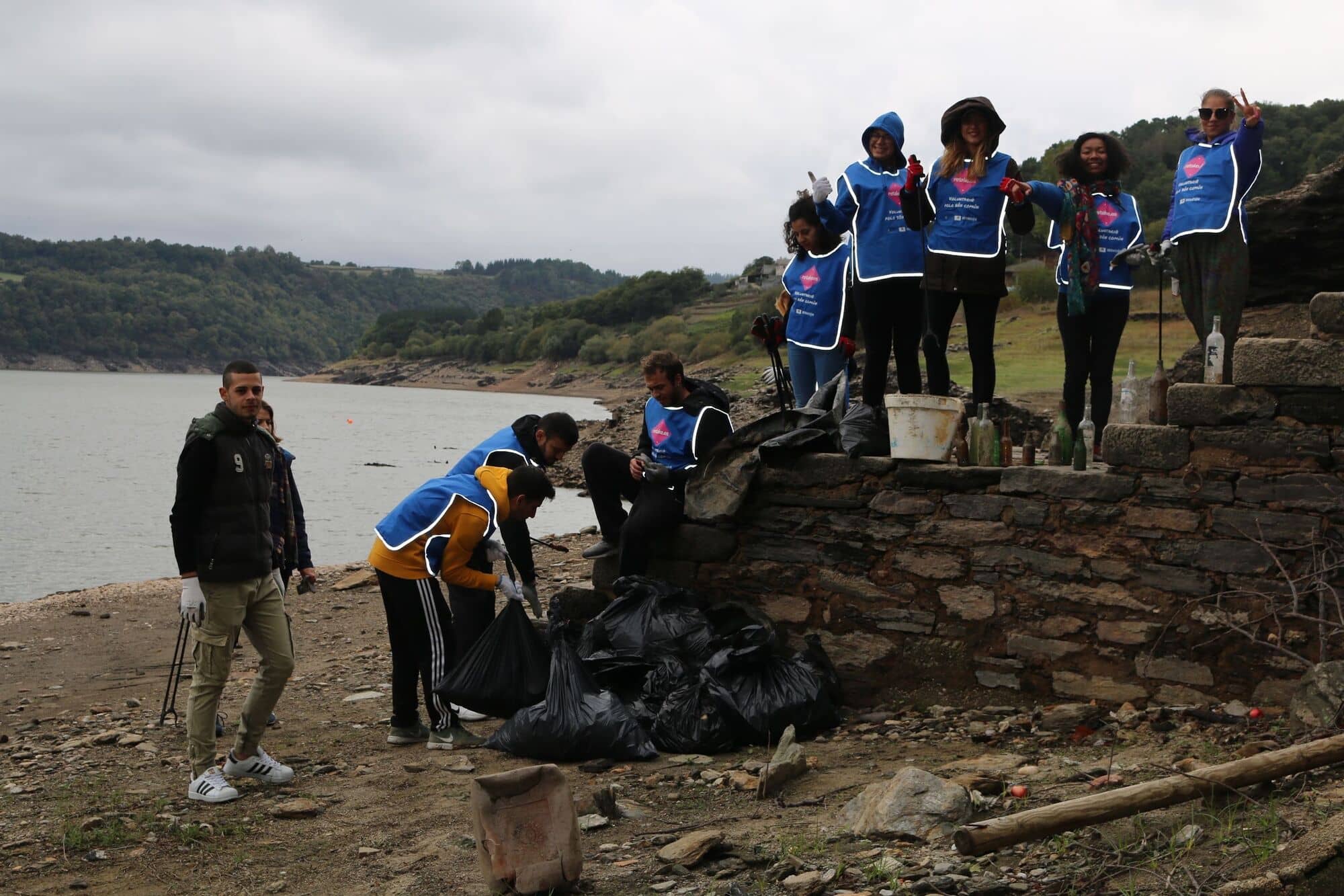 Grupo de voluntarios sobre un muro de piedra junto a un embalse