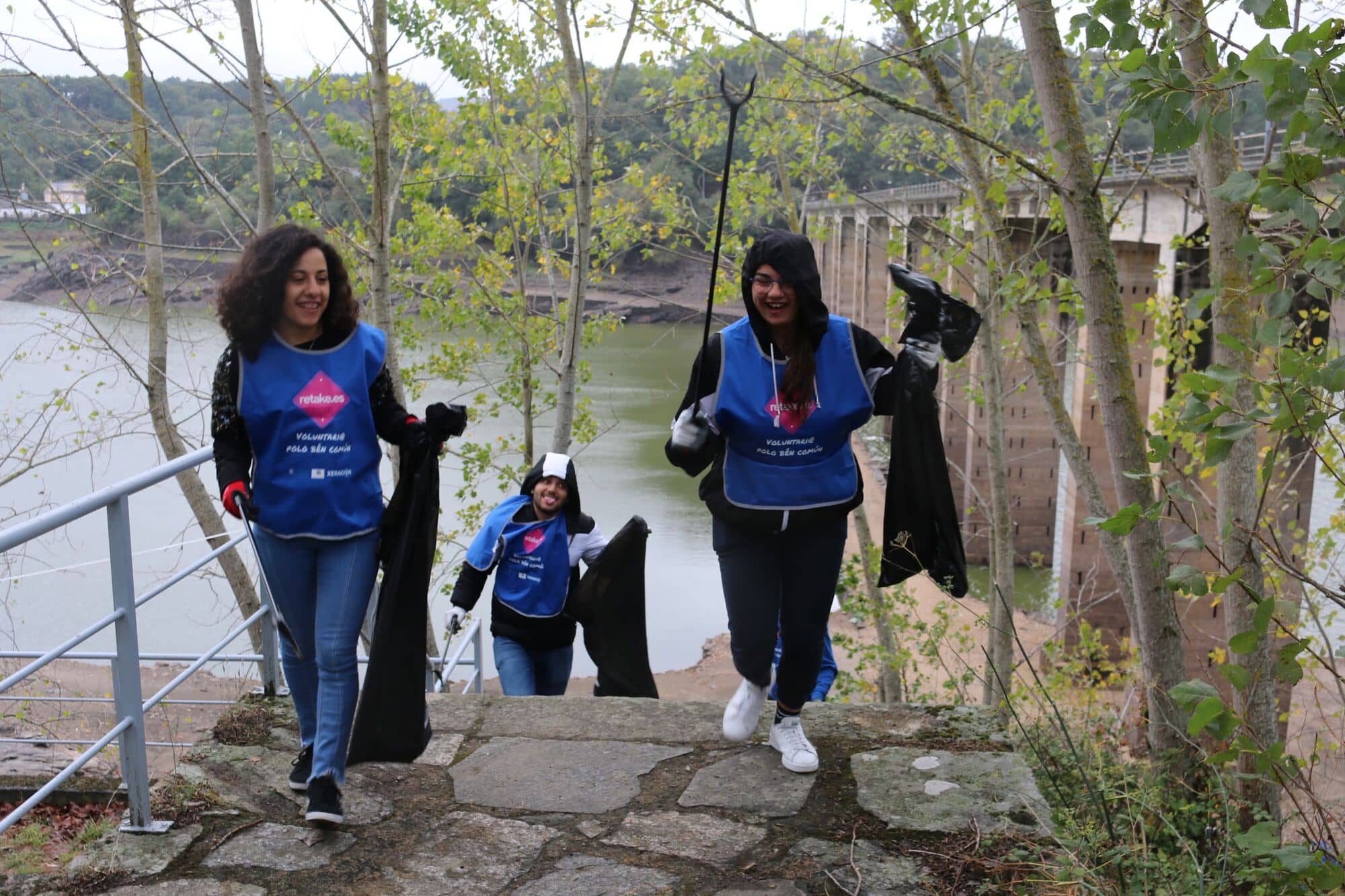 Voluntarias suben unas escaleras junto al río con bolsas
